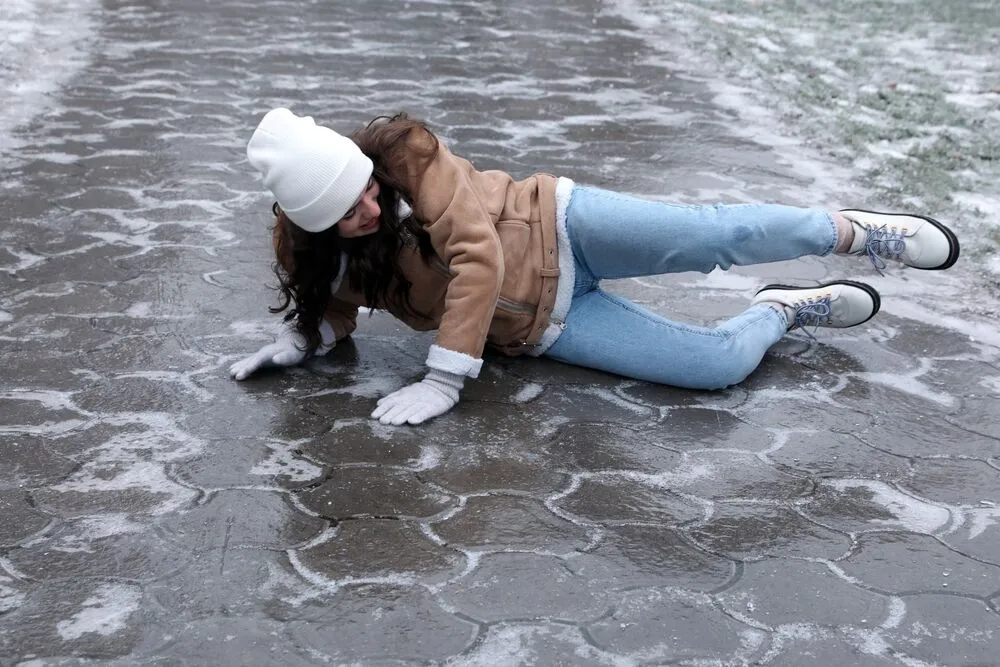 A woman losing her balance due to winter slips and falls on a patch of black ice.